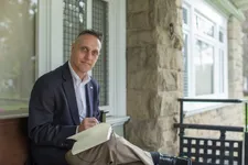 professionally-dressed man writing in a book or journal sitting outside on the doheny campus