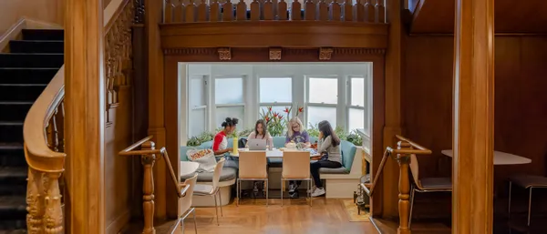 A group of four students studiying at a table with a large wooden staircase in the foreground