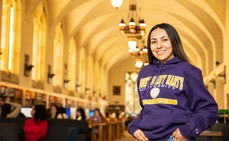 A student standing and smiling with the long Coe Library hall in the background.