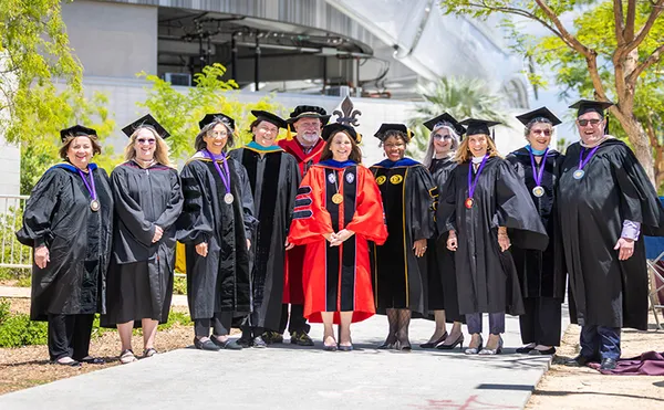 A row of professors in gowns posing in front of a tall building