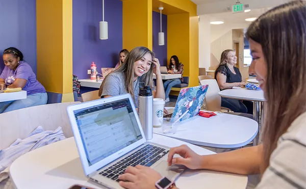 A room of students studying with two students using laptops in the foreground