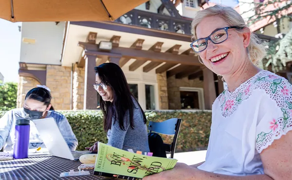 Three students sitting outside reading, one student is smiling at the camera