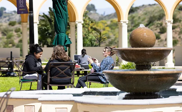 Students sitting around a table talking with a fountain in the foreground