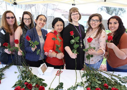 Library staff handing out books and roses at an event.