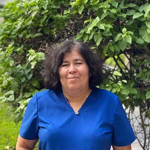 A portrait of a woman with tall hedges in the background.