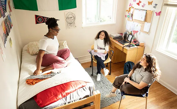 Three students sitting in a bright dorm room and talking.