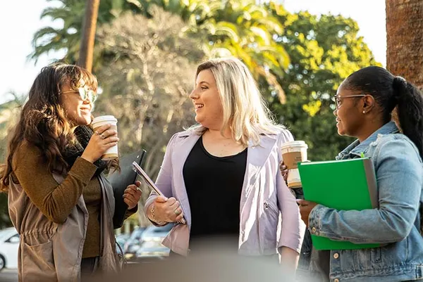 three students standing holding notebooks talking