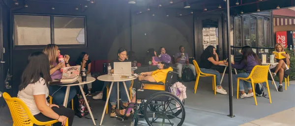 Many students sitting around tables outdoors and talking, studying, laughing