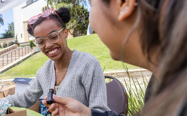 Two students smiling while writing with markers at an event booth