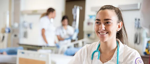 nursing student in white coat smiling while working in classroom lab