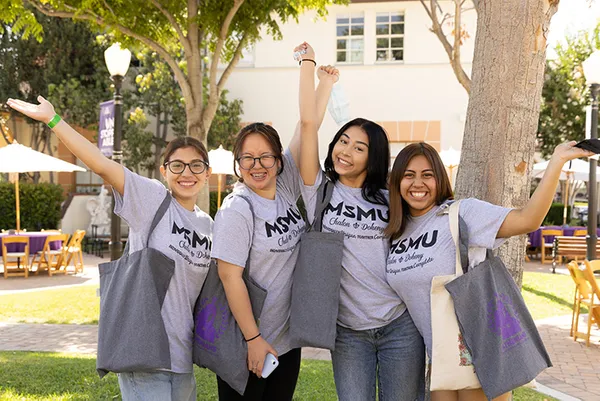 Four students smiling and posing outside under a tree.
