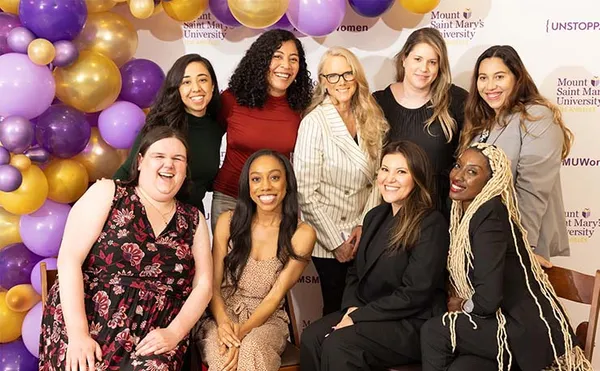 group of alumnae smiling together with purple and gold balloon arch