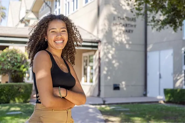 female student standing in front of campus building smiling
