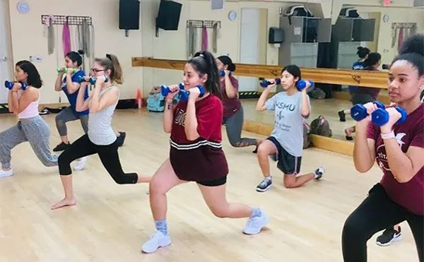 Students lunging while holding weights in an exercise room