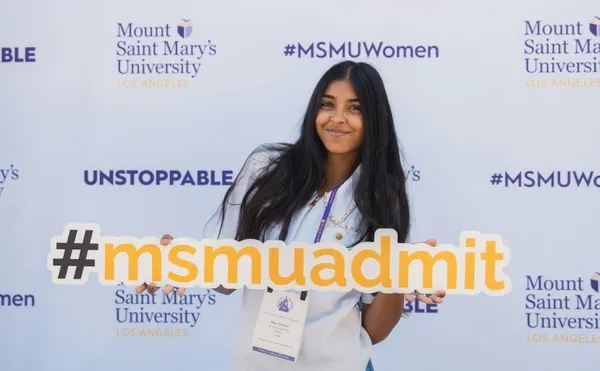 A student smiling in front of a photo wall holding a #msmuadmit sign