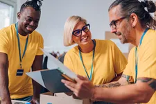 three volunteer workers in yellow shirts smiling and working together over some paperwork