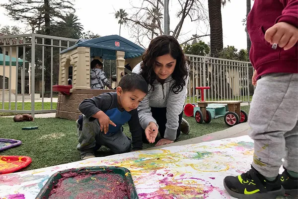 staff kneeling with a student painting on the ground