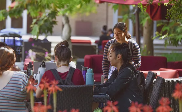 A small group of students studying outside under umbrellas.