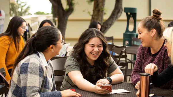 group of female students sitting outdoors at the Chlaon campus looking at phone and laughing together.